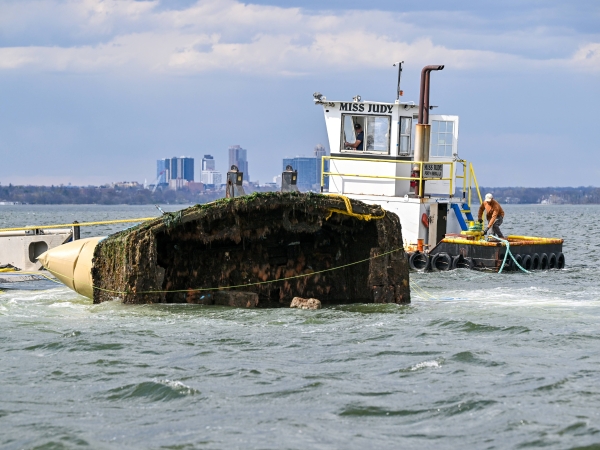 People removing a half sunken vessel from a waterway.