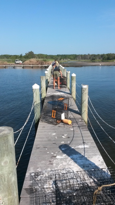 Two people stack crab traps at the end of a dock.