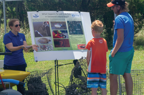 Three people stand around a poster talking about derelict crab traps.