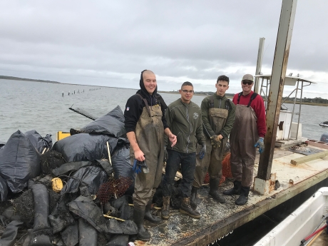 Four project participants stand on a dock next to bags of collected debris.