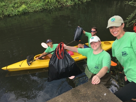 Project participants on shore and in a kayak pose with bags of debris collected from One Mile Creek.