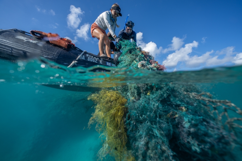 Two people pulling up derelict fishing gear on to a boat.