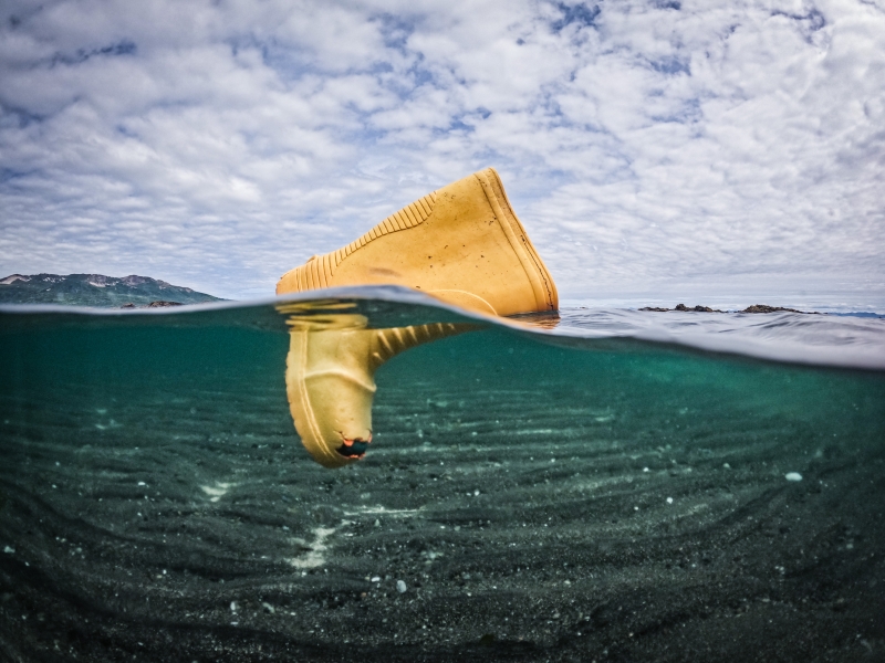 A yellow rainboot floating at the surface of the water with a view from underwater and above the surface.