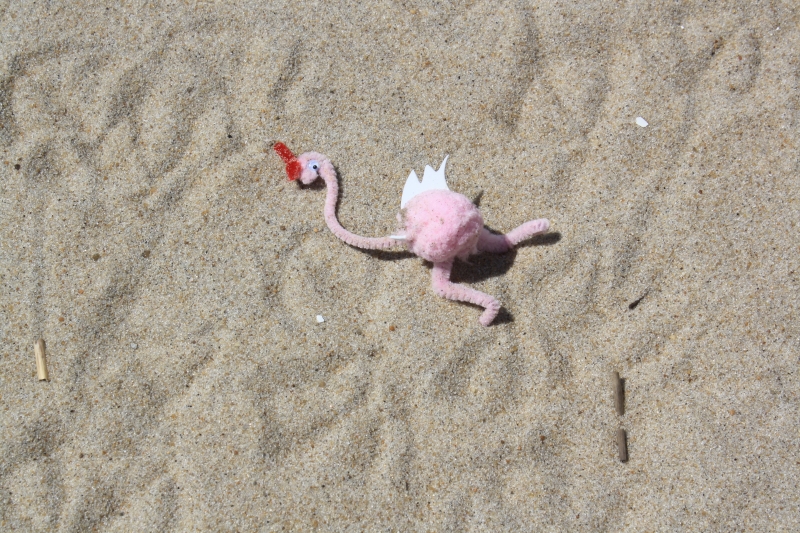 Pink flamingo decoration made out of pipe cleaners on a beach.