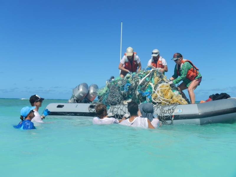 People in a small boat and in the water hauling derelict nets into the boat.