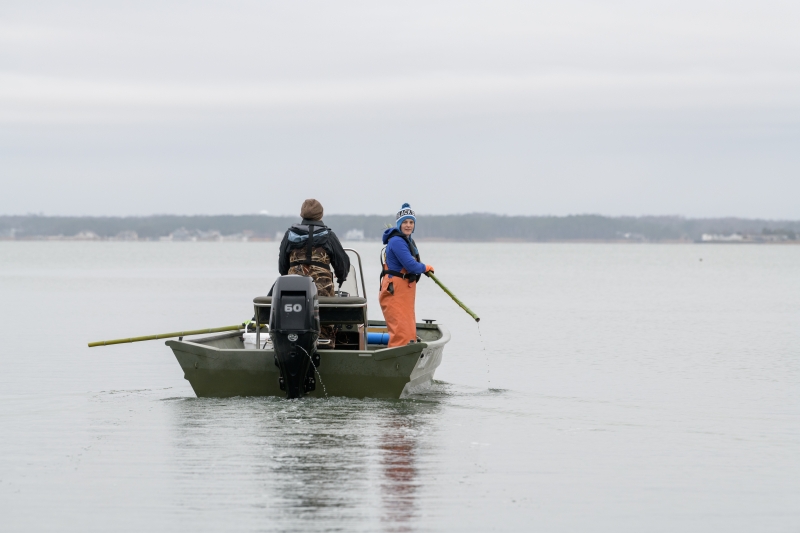 Two people stand in a boat holding long pole that will be used to lift crab pots out of the water.