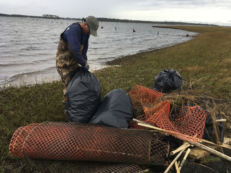 A project participant stands near a pile of debris while securing a bag of collected debris.