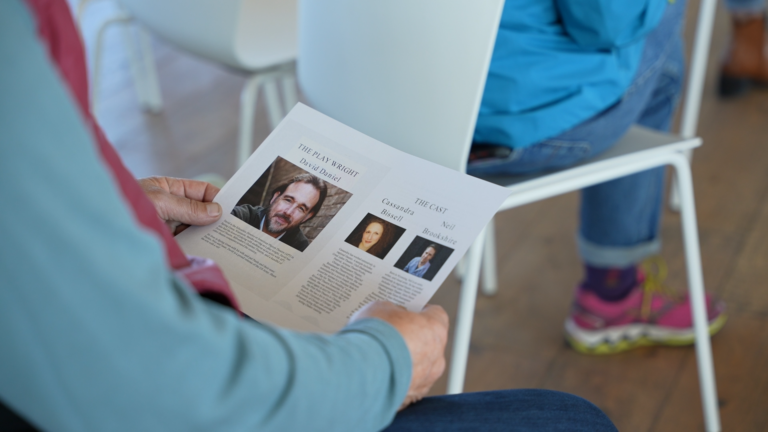 A person wearing long blue sleeves reads about the playwright and the cast list within the program for “Me and Debry.”