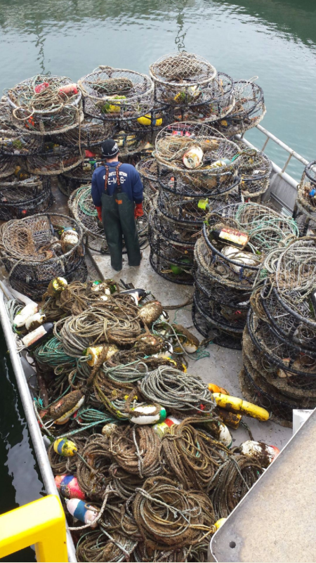 A man stands on a boat surrounded by many derelict crab pots and lines.