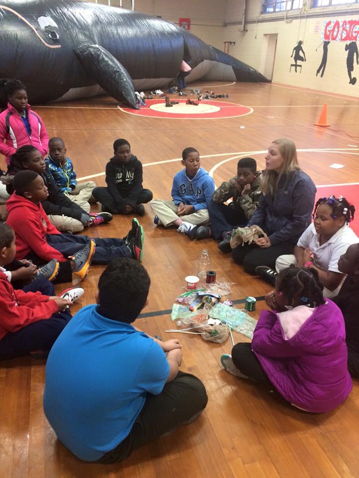 Students sit on the floor in discussion with the inflatable whale classroom in the background.