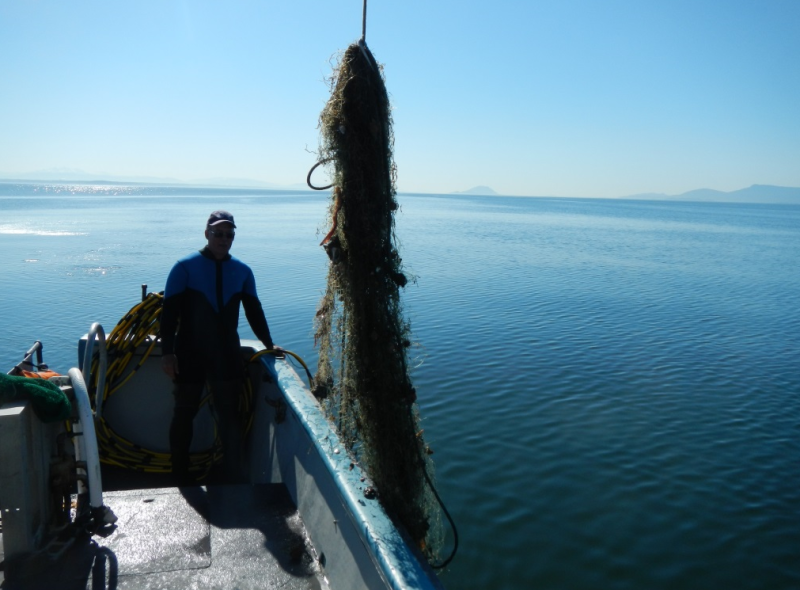 A person on a boat standing next to a derelict net.